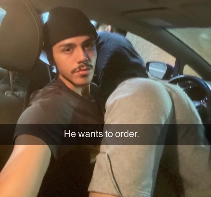 a man in the driver's seat of a car has another man leaning over him with his butt facing the camera